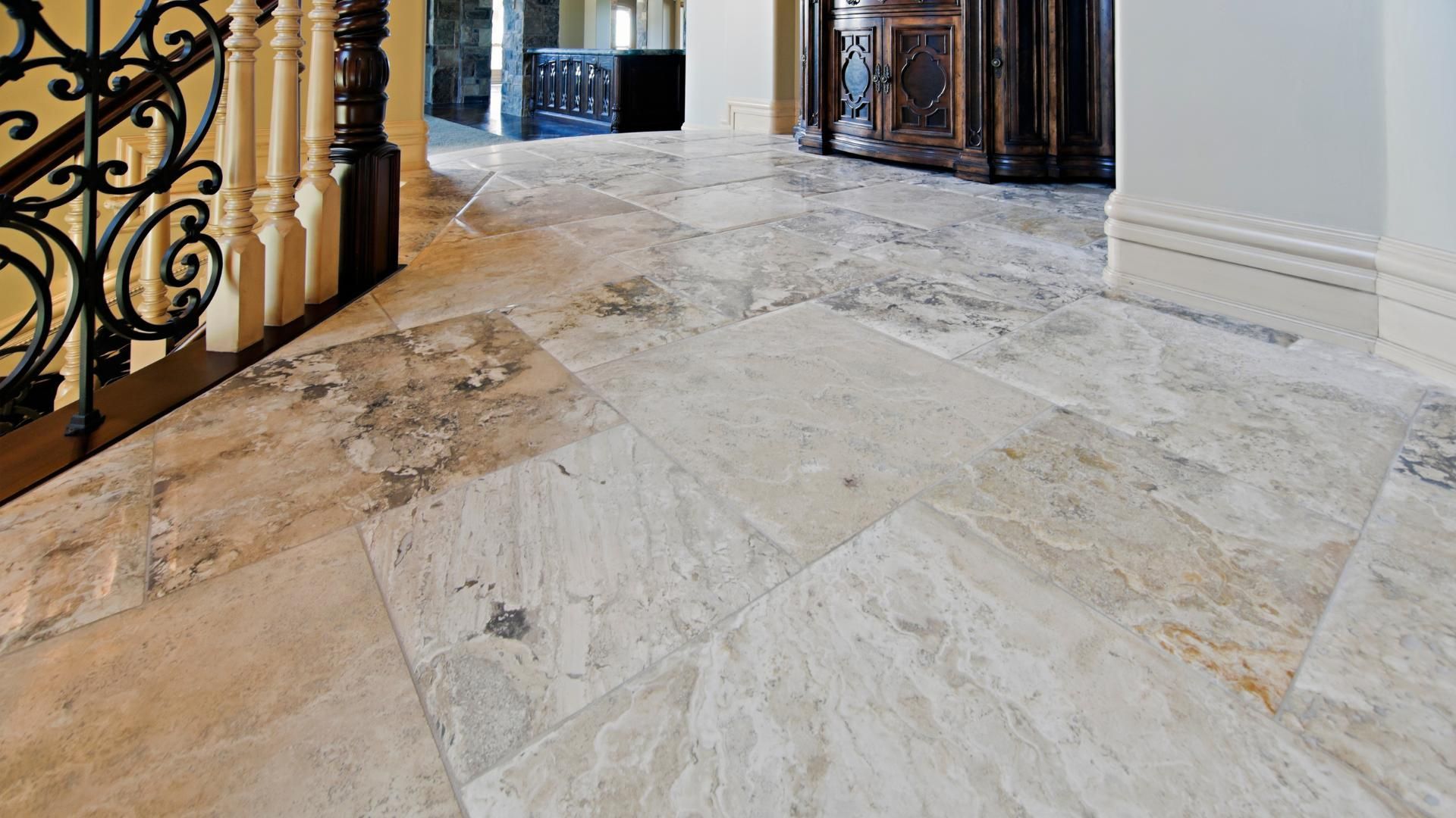 Travertine tile flooring in entryway, next to stairs with wrought iron railing.