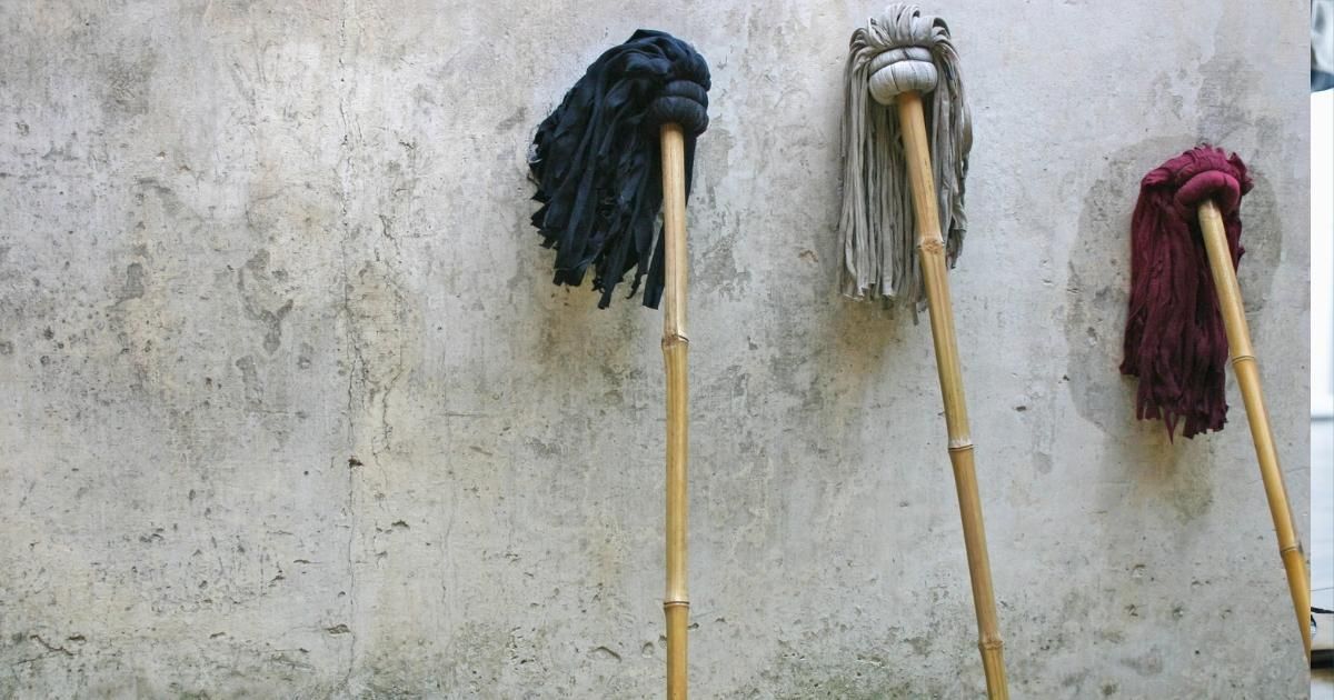 Three mops with dark, white, and red heads leaning against a weathered wall.