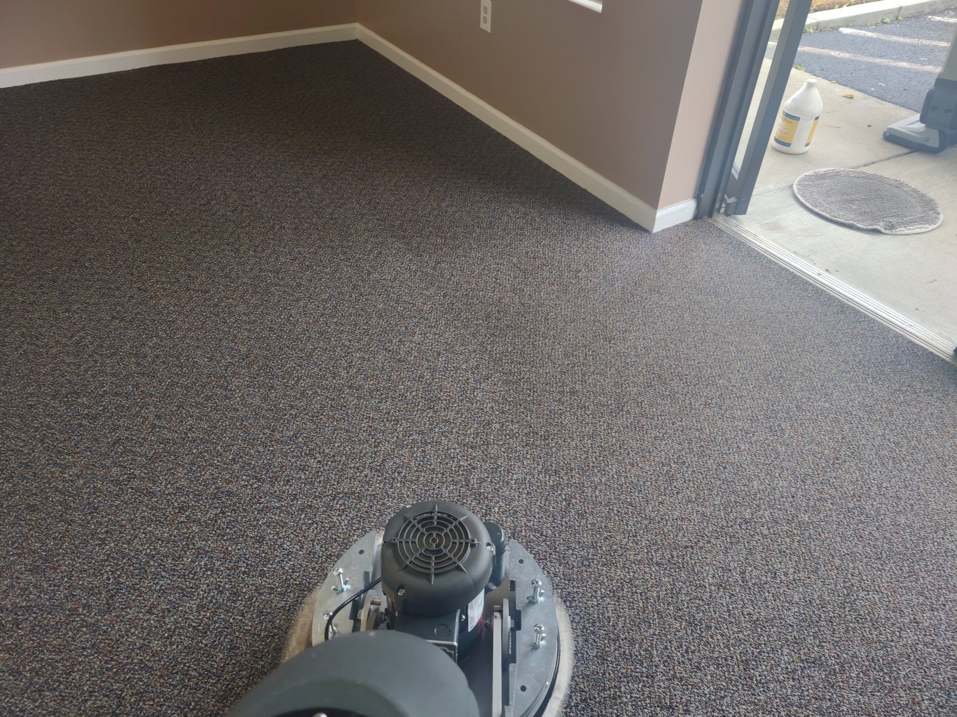 A carpeted room being cleaned with a floor buffer; brown walls, white trim, open doorway to the right.