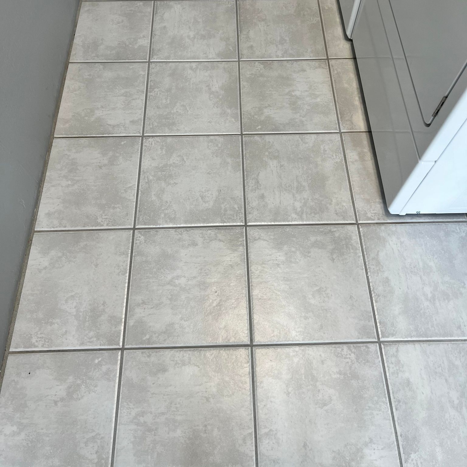 Light gray tiled floor next to a white appliance and a gray wall.