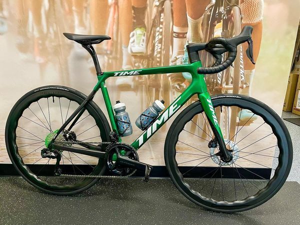 Green TIME road bike with black wheels and water bottles, displayed indoors.