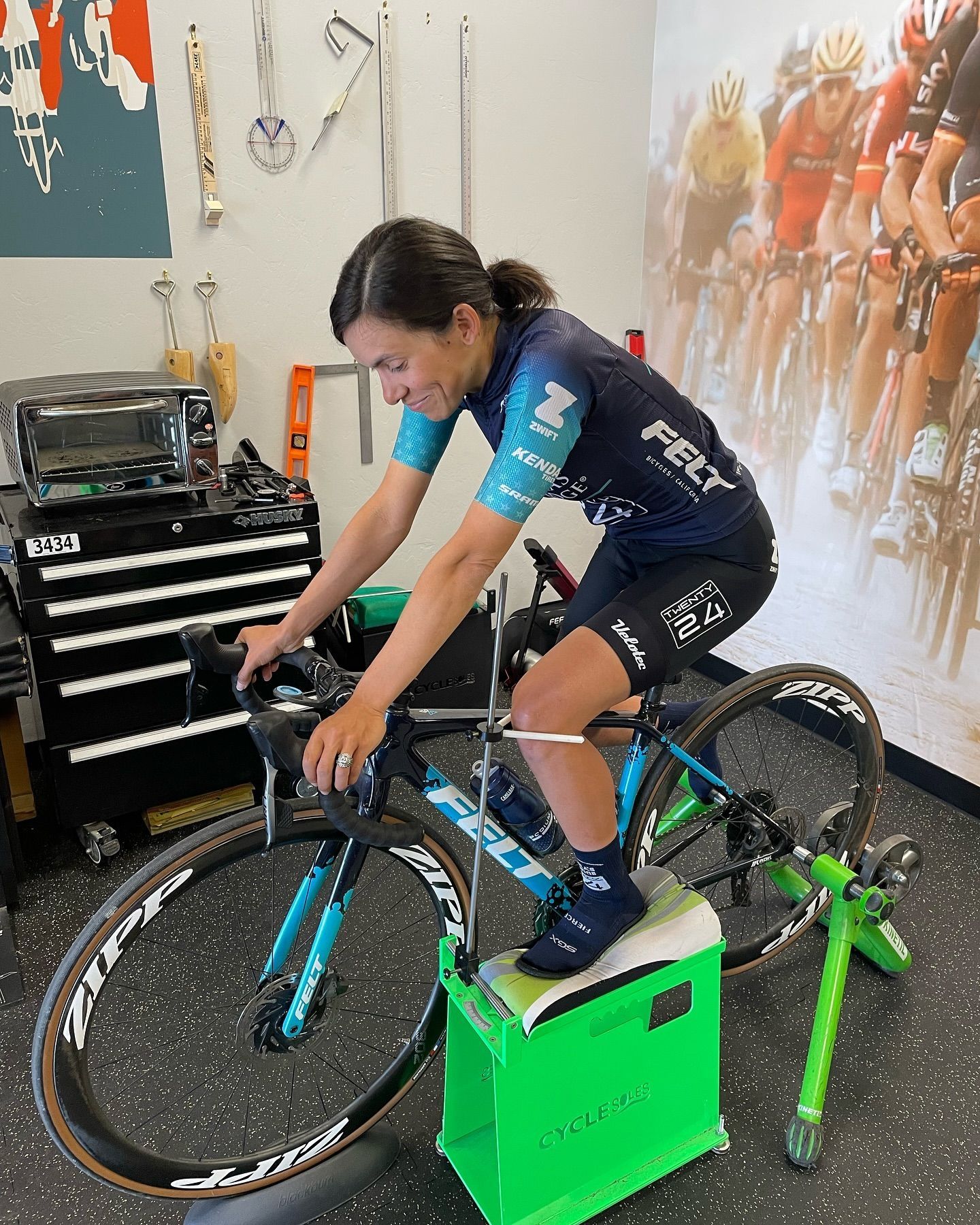 Woman on a stationary bike in a bike shop, testing posture. Wearing cycling gear. Green and black bike.