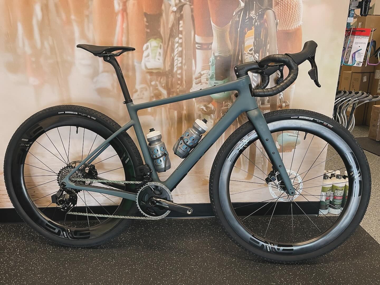 Gray gravel bike with black wheels and tires, two water bottles, and disc brakes.