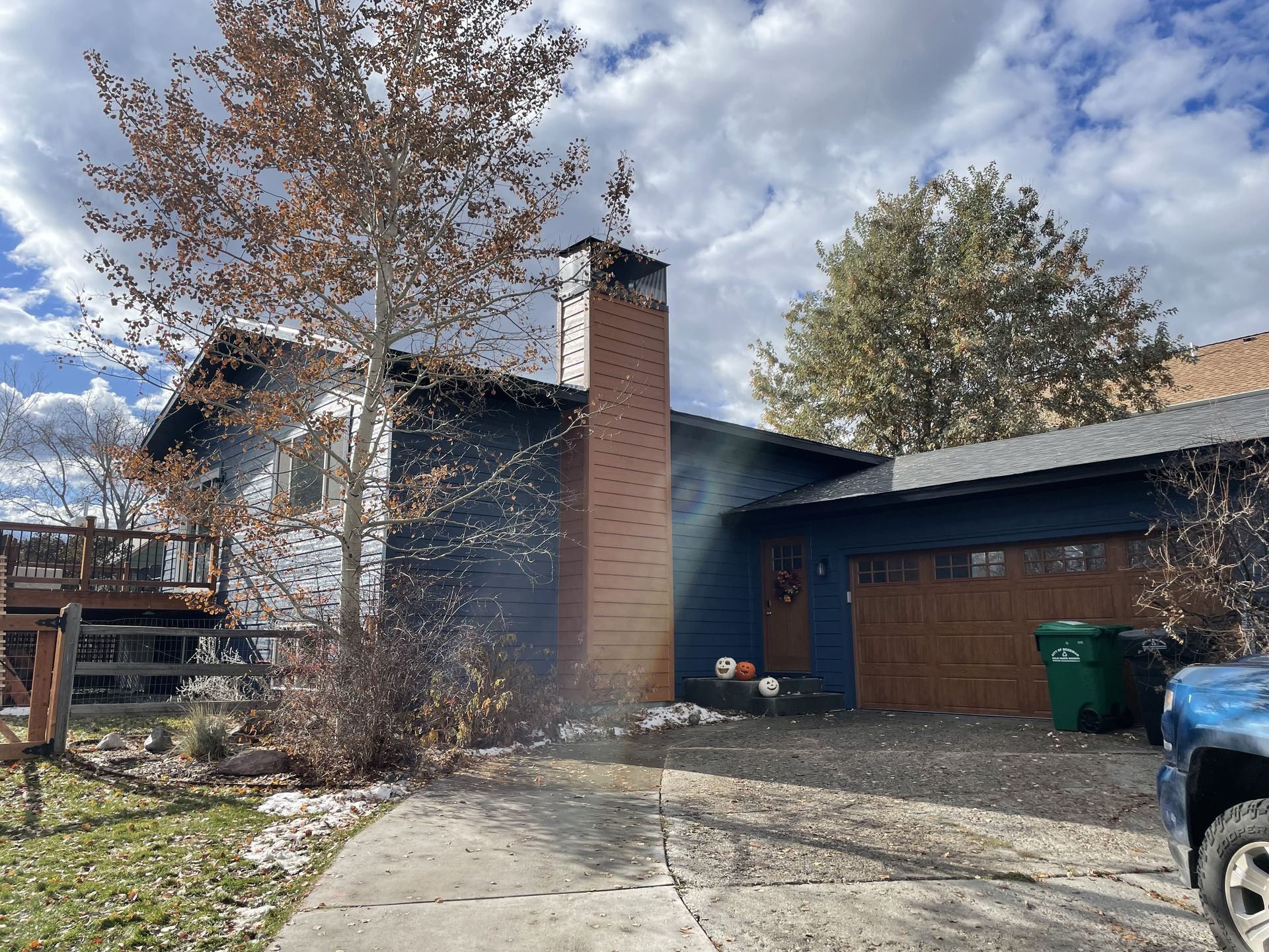 Suburban house with a brick chimney, garage, and trees, with smoke or steam near the driveway.