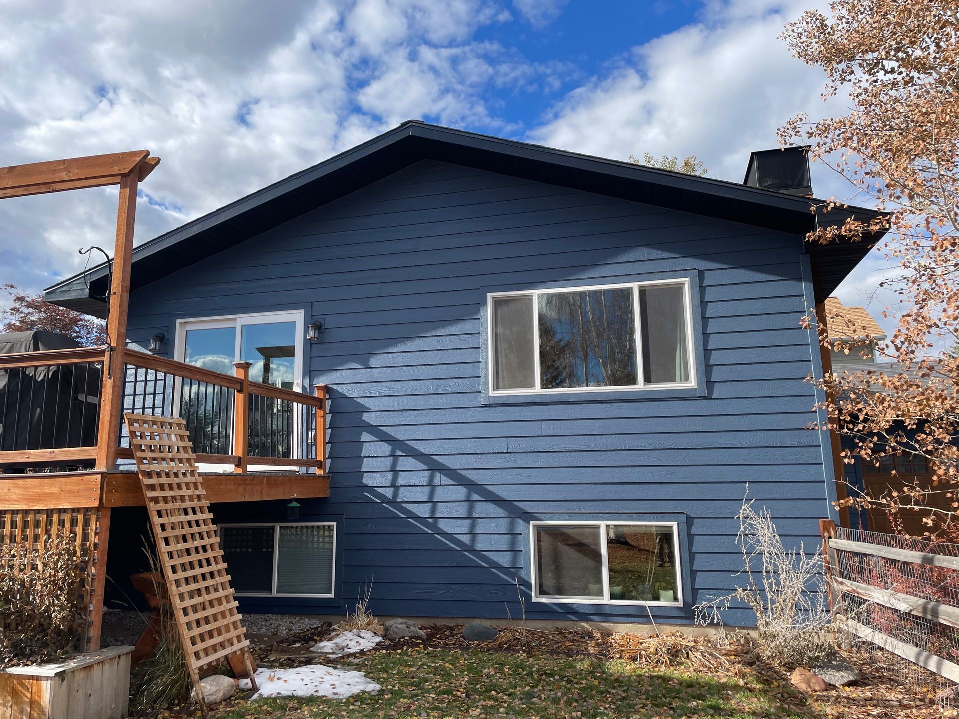 Blue house with a wooden deck and staircase in a fenced backyard