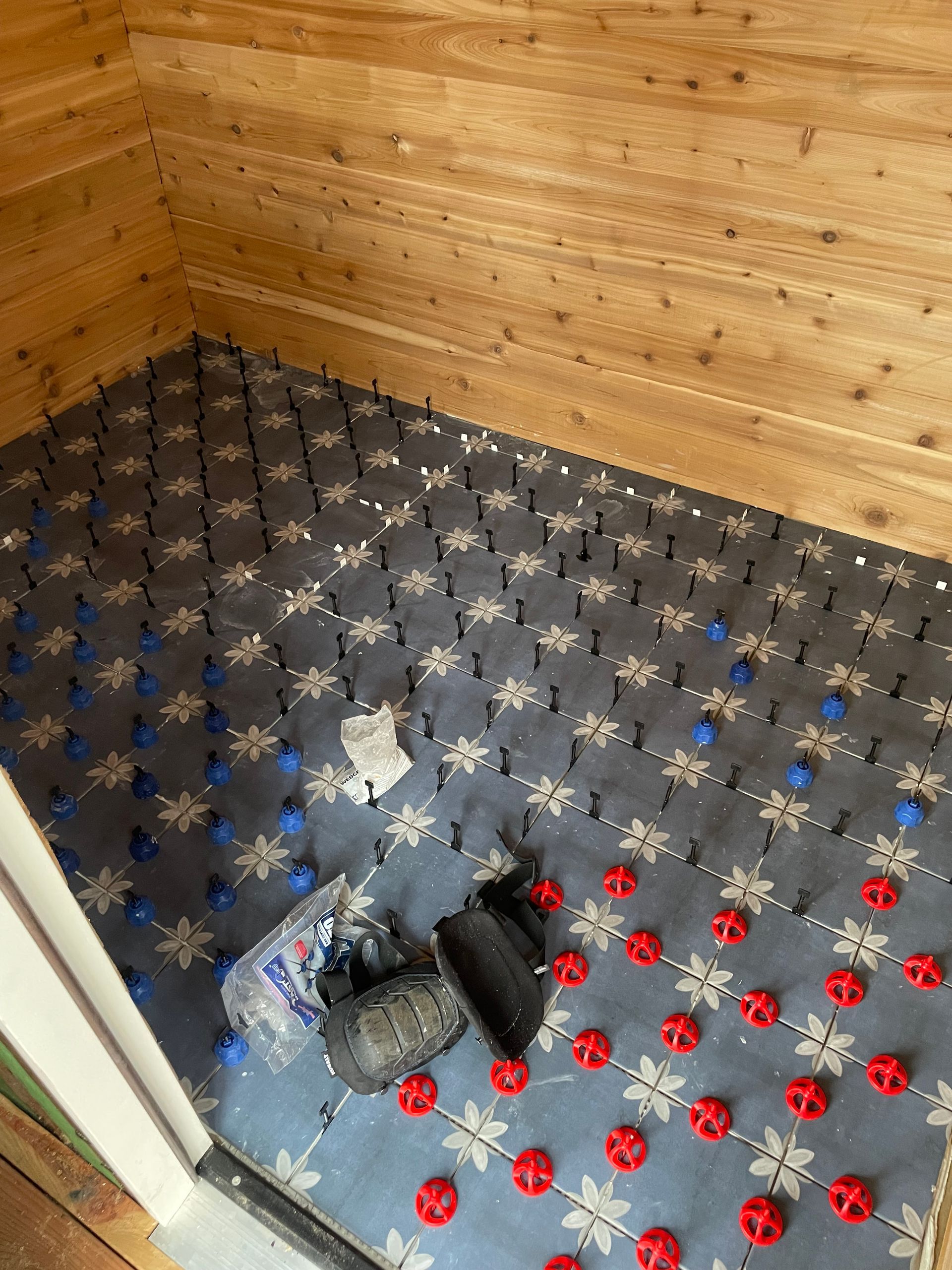 Small room with wood-paneled walls and black floor tiles; gloves and shoes lie on the floor near a doorway.
