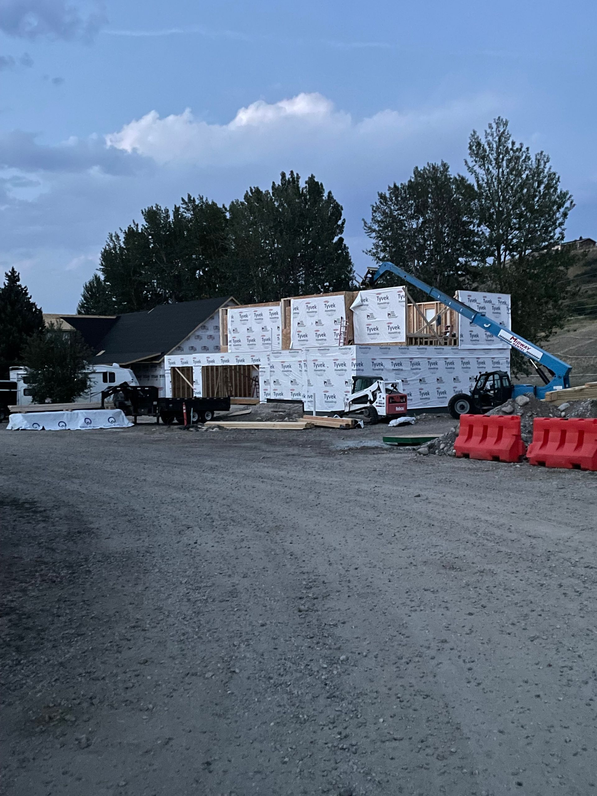 Partially built house wrapped in white insulation, with gravel foreground and construction materials at dusk