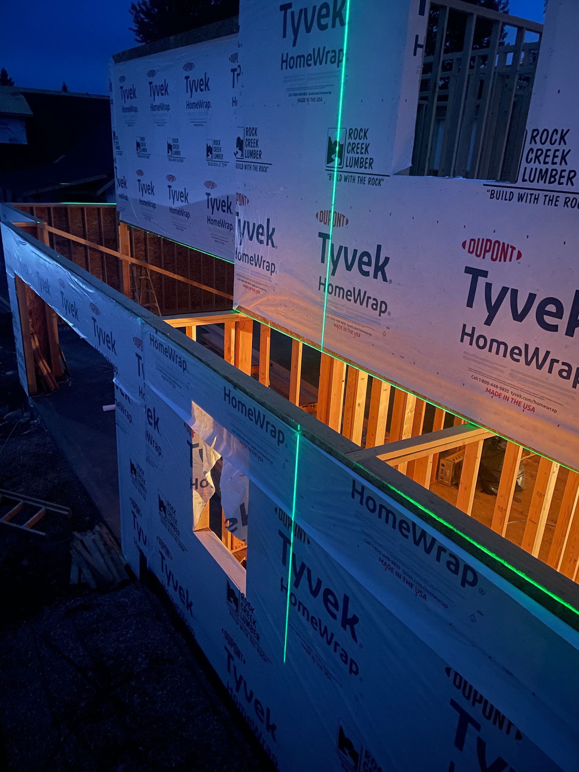 Partially built home framed in blue light, wrapped in Tyvek house wrap at dusk with warm interior glow