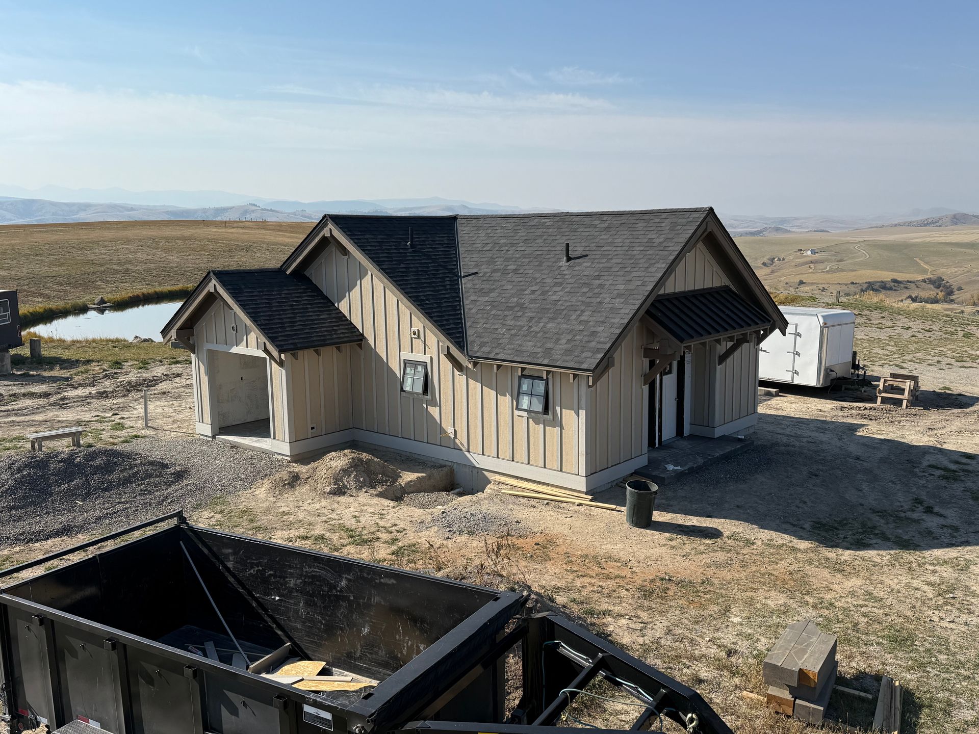 Small tan house with dark roof in a dry rural landscape, with a black structure in the foreground.