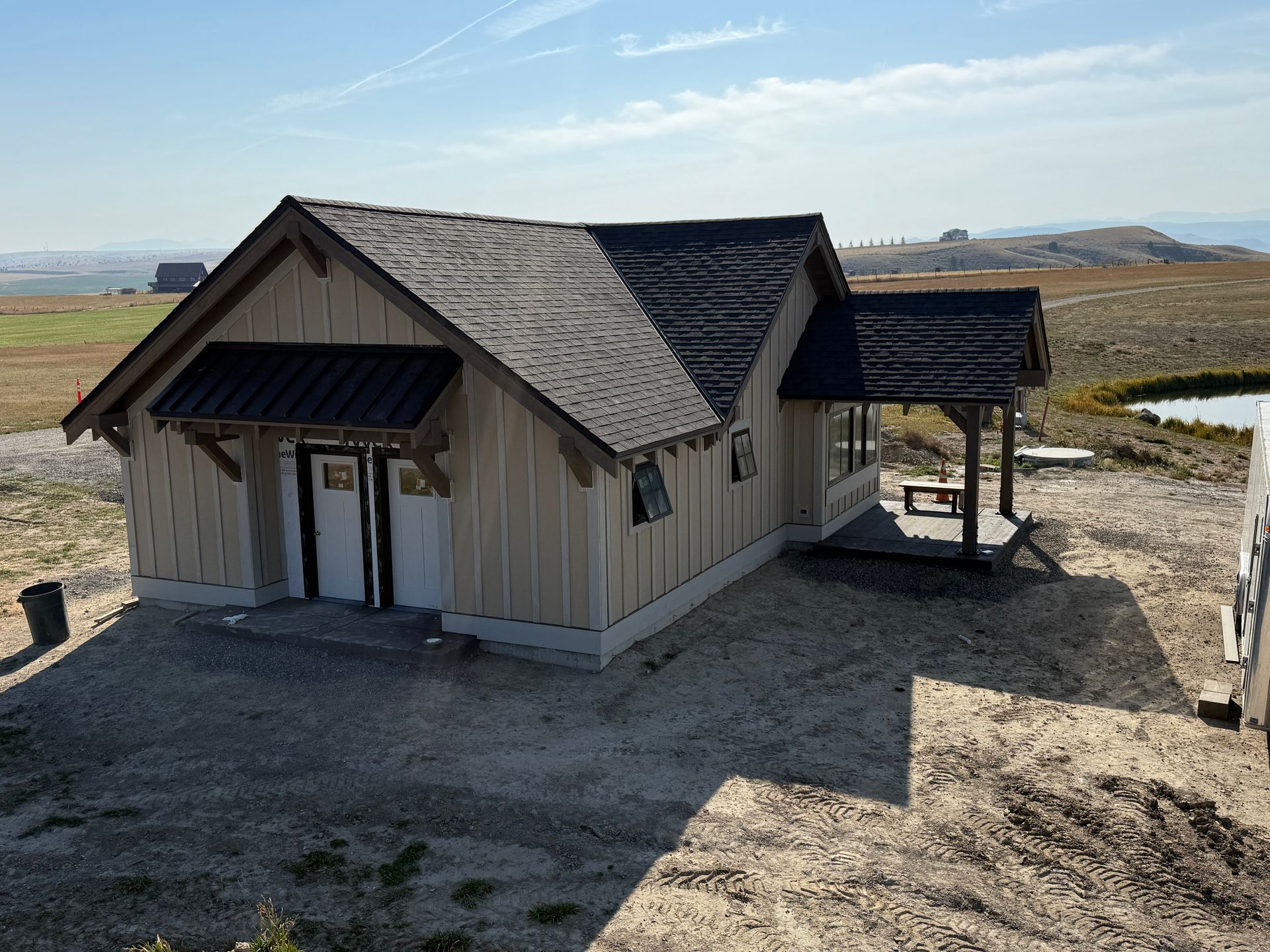 Small beige cabin with a dark roof on a gravel site in a wide open desert landscape.