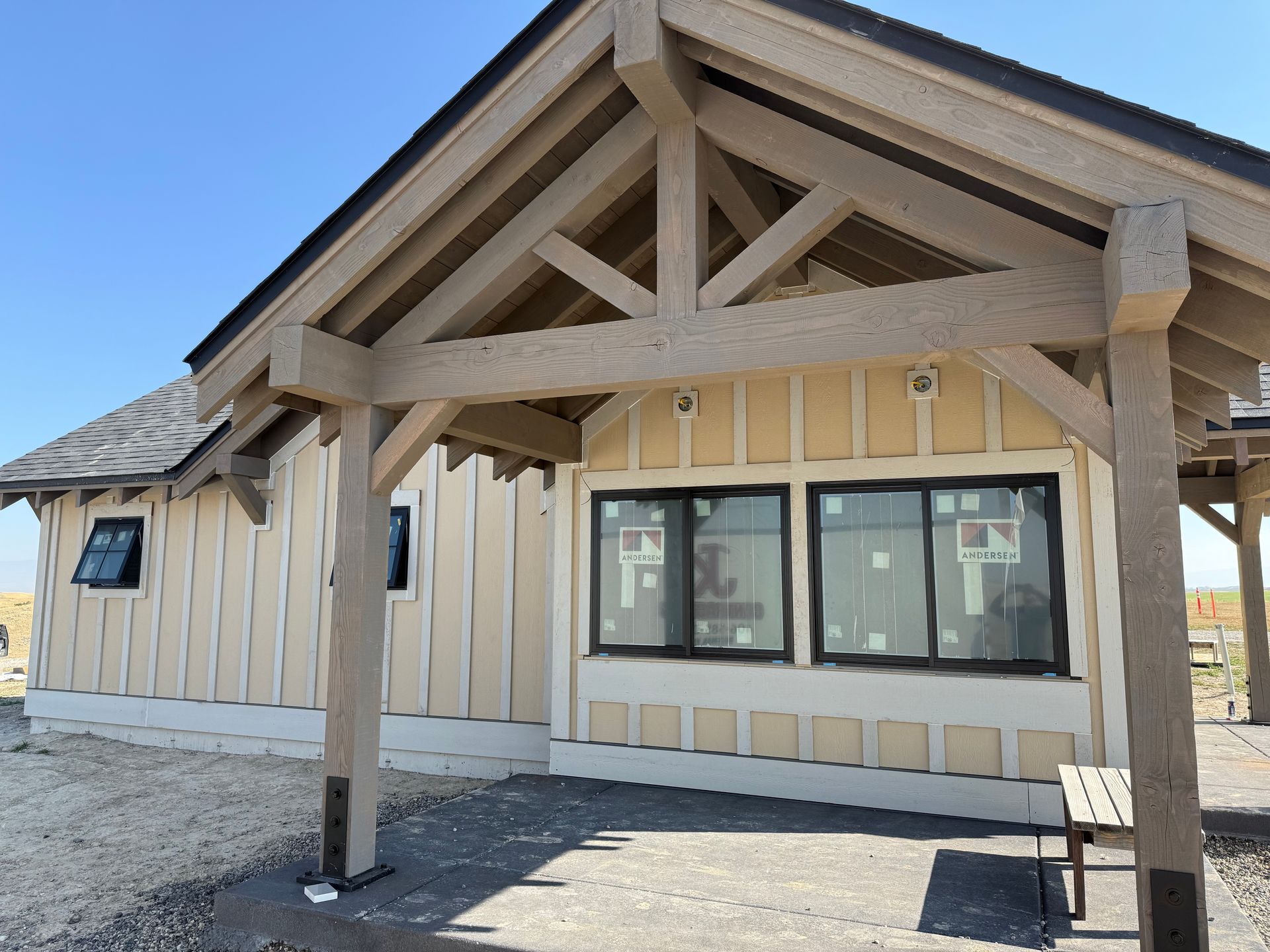 Exterior of a small beige building with a timber porch and dark-framed windows under a gabled roof.