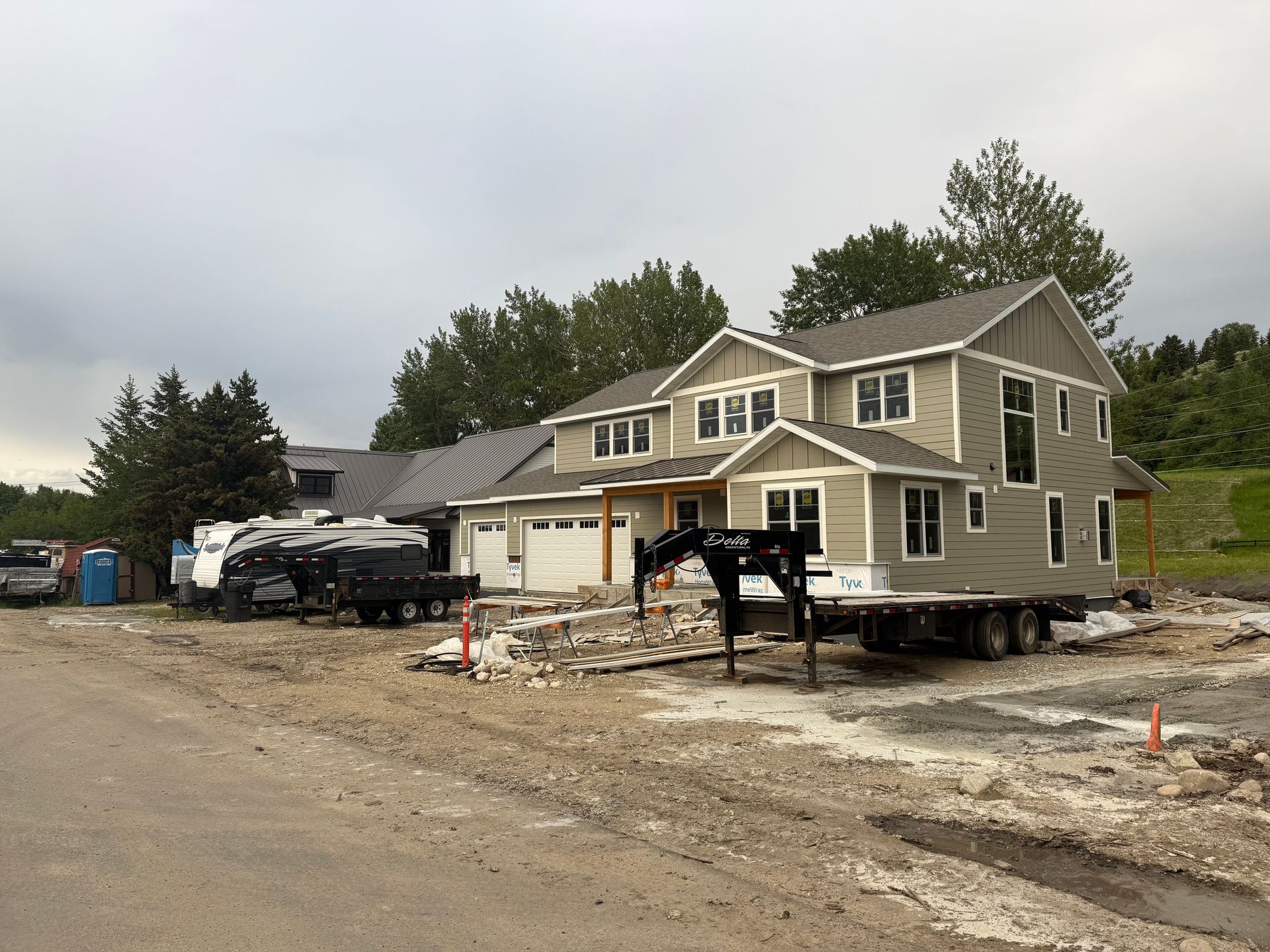 House under construction with workers, construction vehicles, and debris along a dirt road