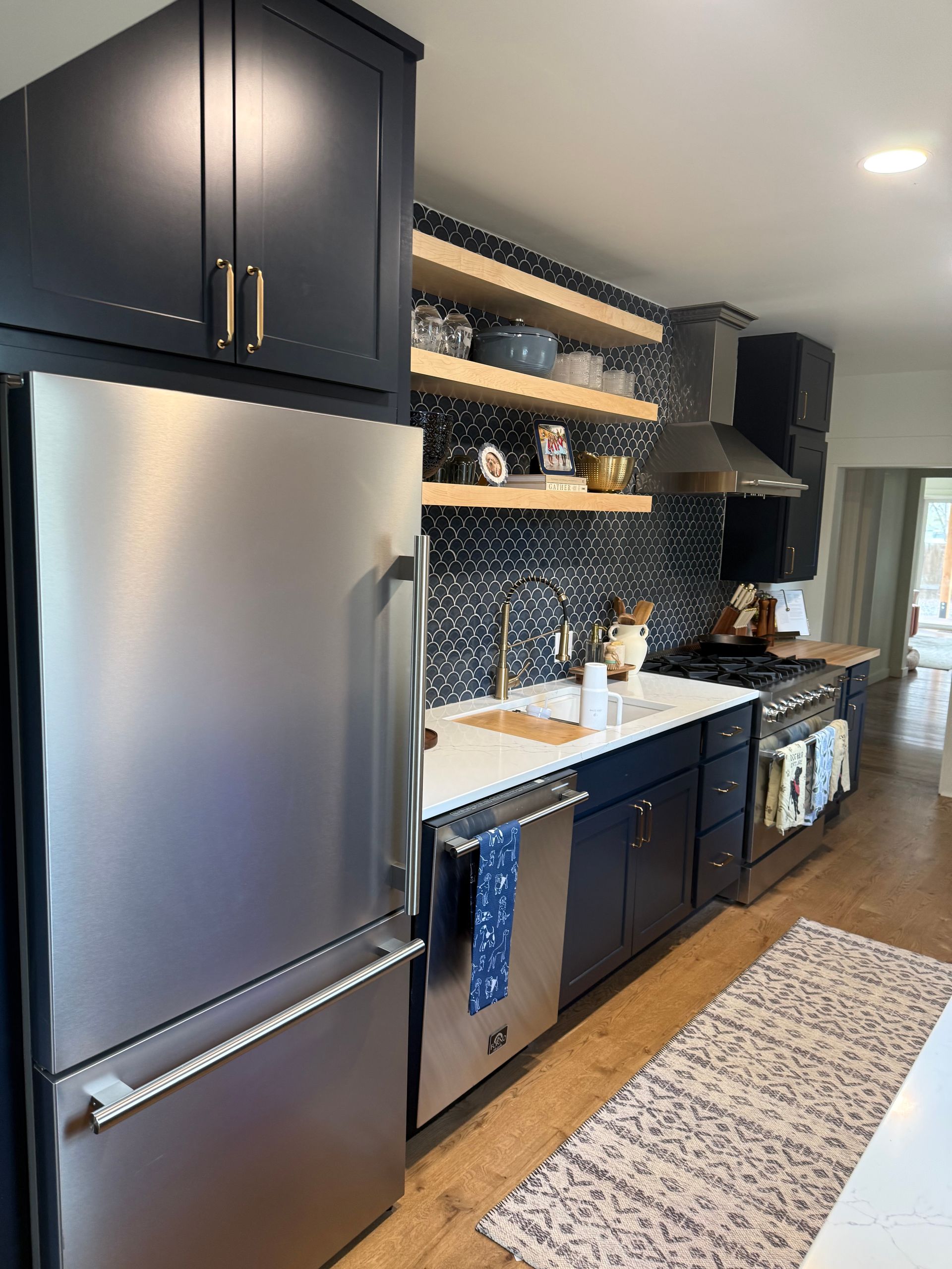 Modern kitchen with stainless steel fridge, dark cabinets, open shelves, and white countertops