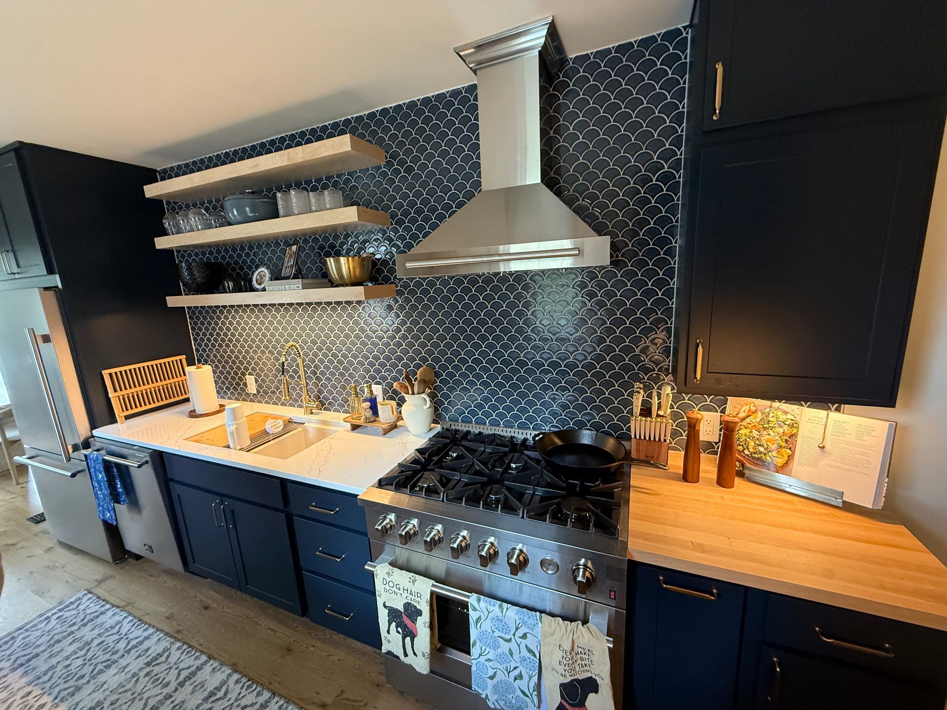 Modern kitchen with dark cabinets, patterned backsplash, stainless range hood, and wood countertops