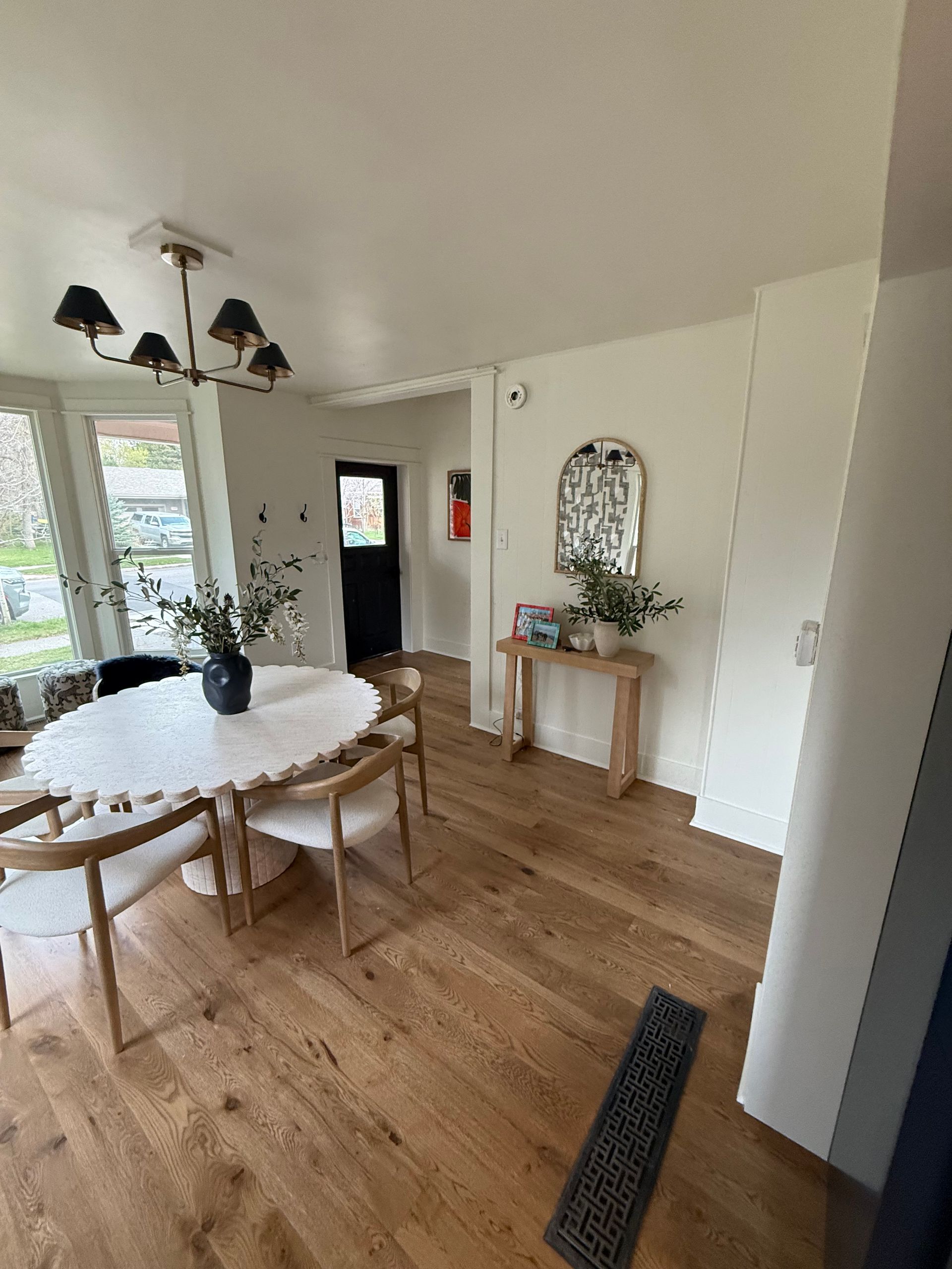 Bright dining room with round white table, wooden chairs, chandelier, and console table by a mirror.