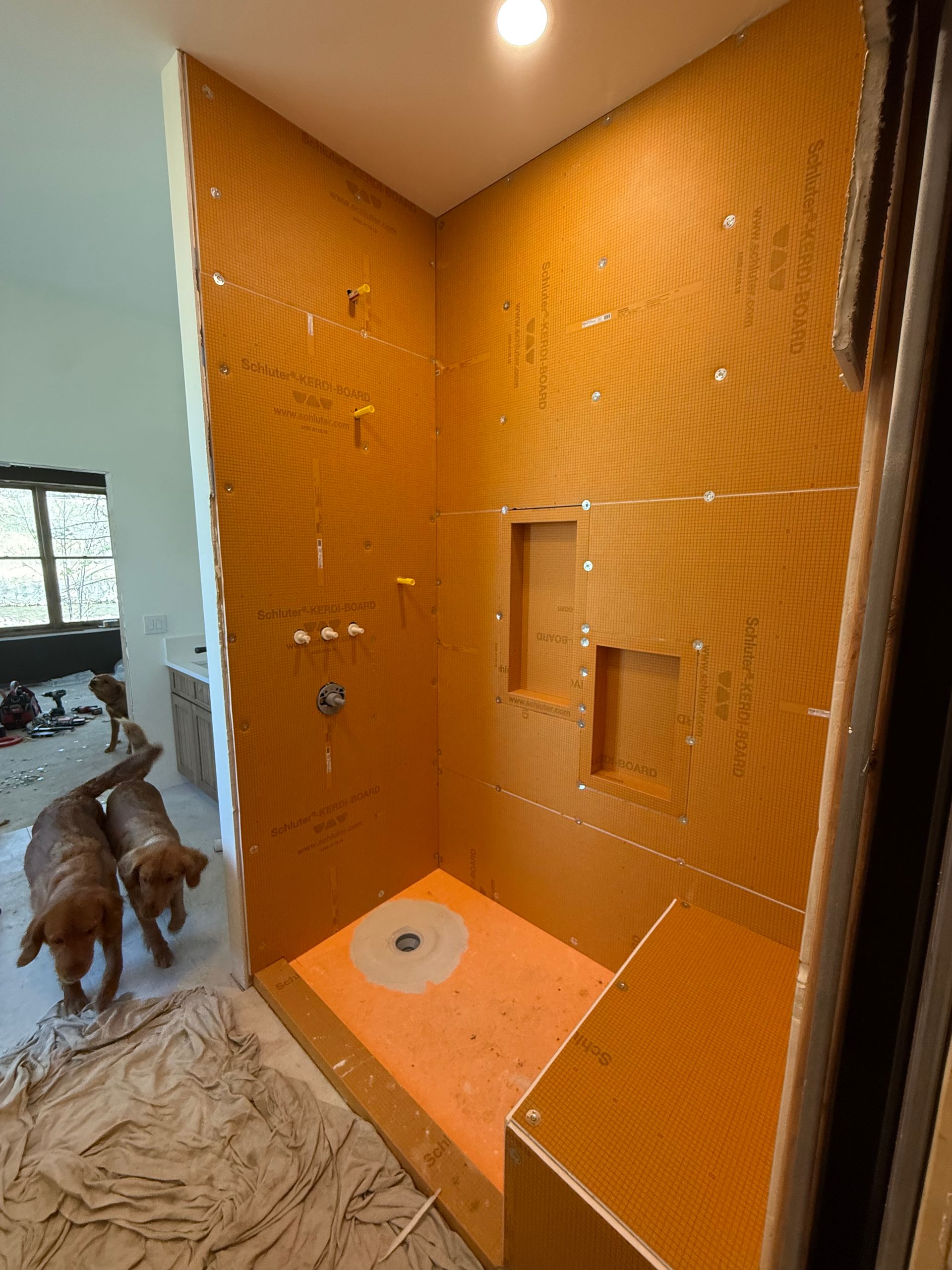 Orange-tiled shower stall with a built-in shelf and drain, viewed from an open bathroom doorway.