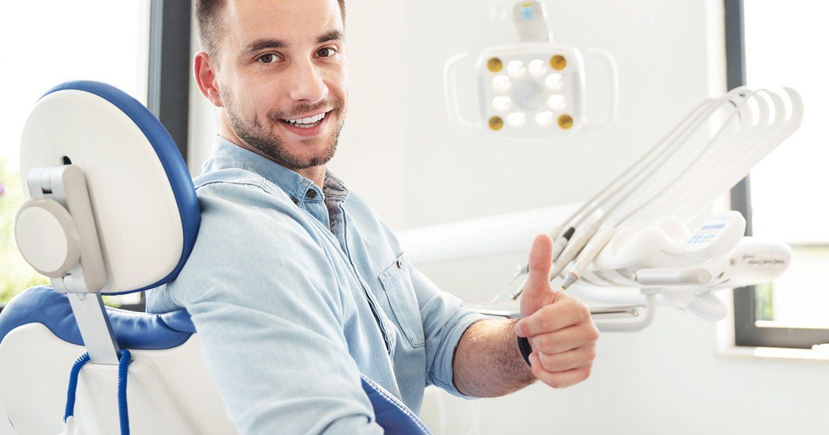 A man is sitting in a dental chair and giving a thumbs up.