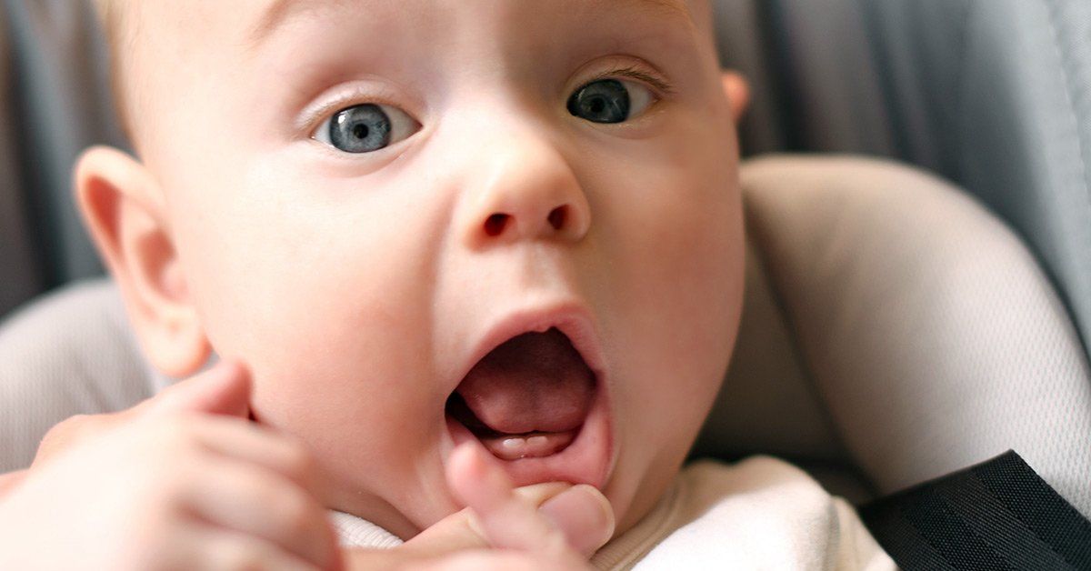 A baby is sitting in a car seat with his mouth open.