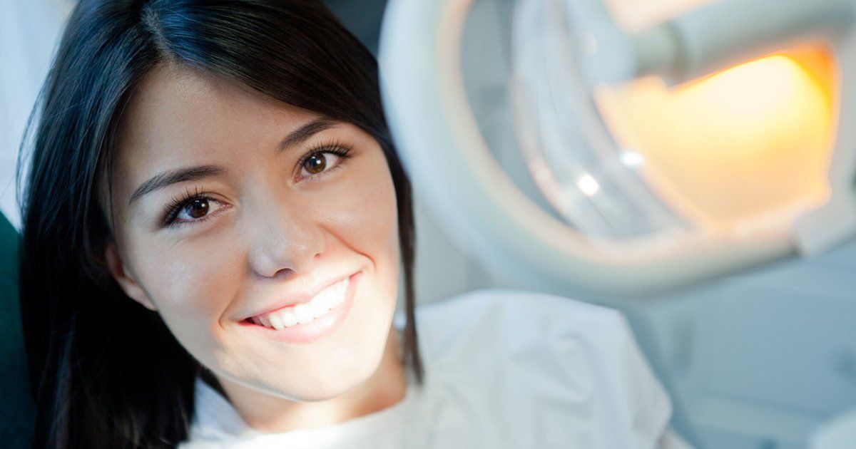 A woman is smiling while sitting in a dental chair.