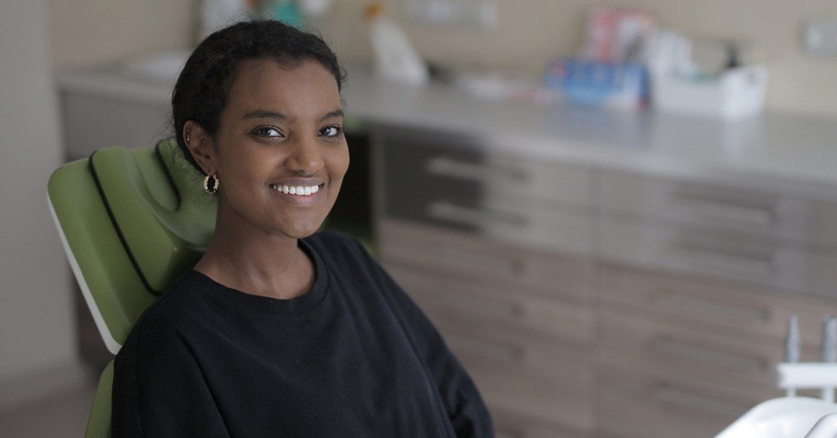 A woman is smiling while sitting in a dental chair.