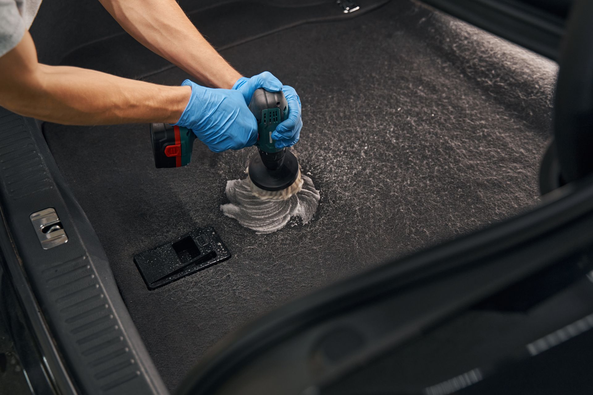 Person in blue gloves using a tool to clean a car's interior carpet.