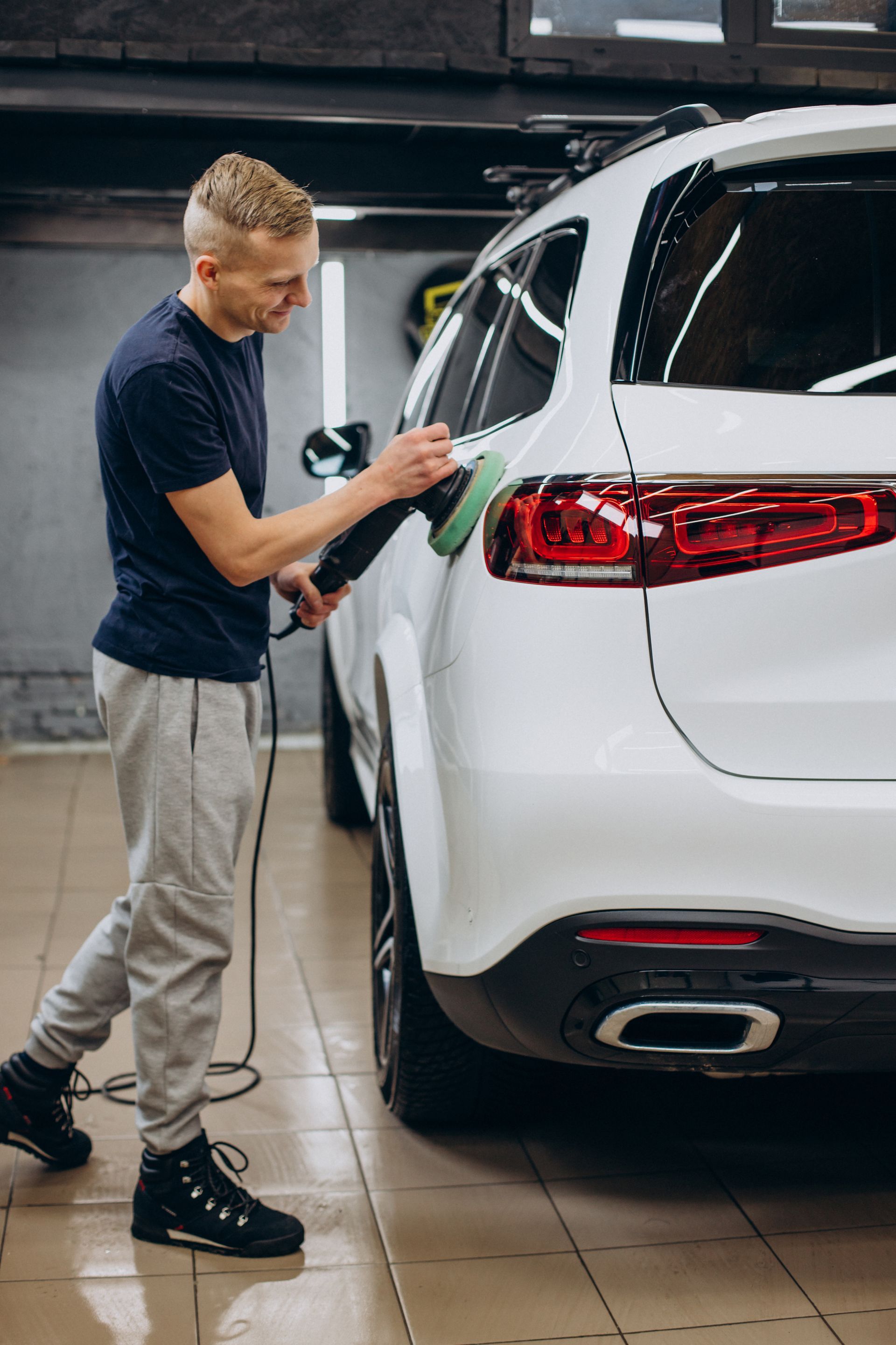 Man polishing a white SUV with a machine in a garage.