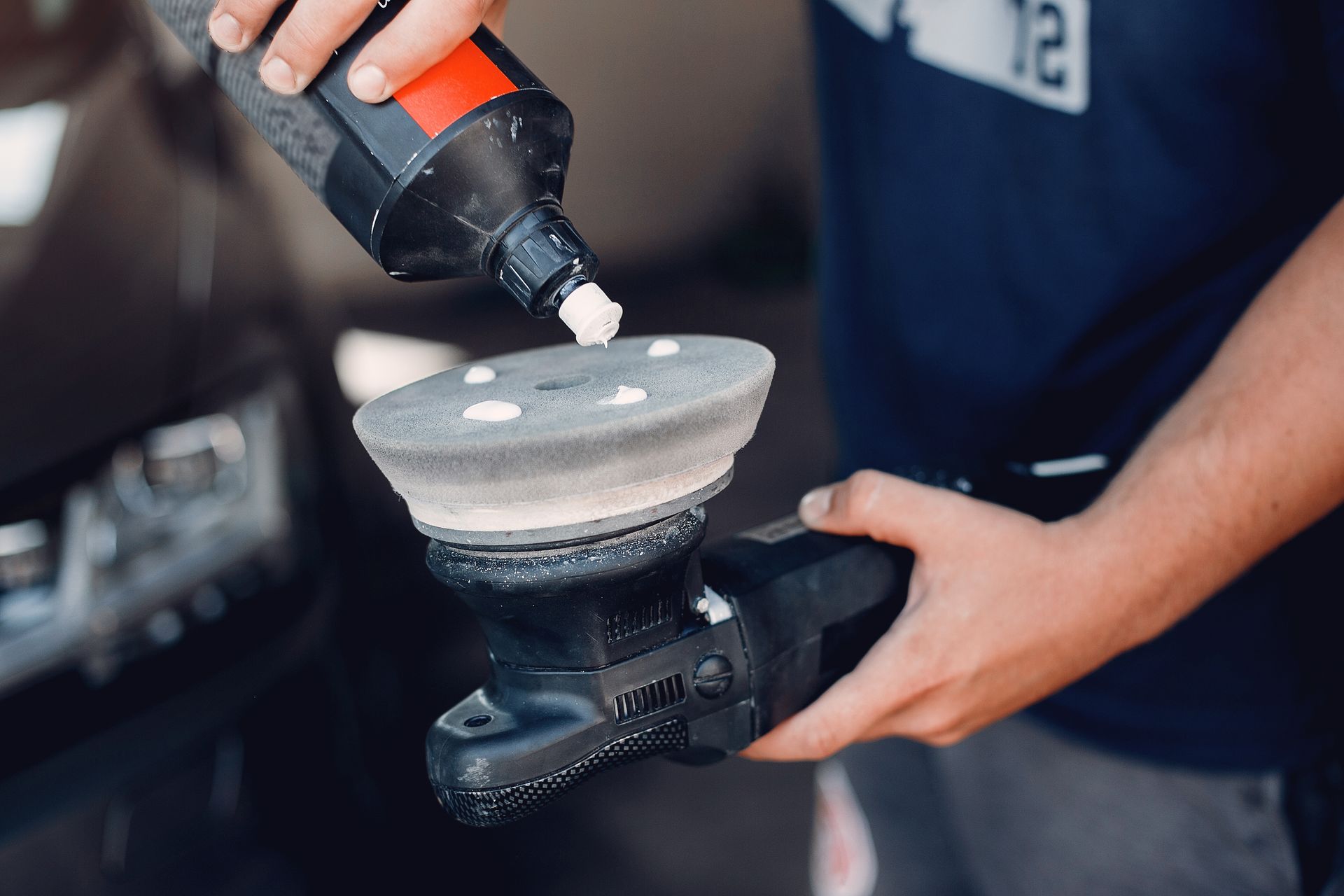 Person applying car wax with a blue applicator to a gray car door.