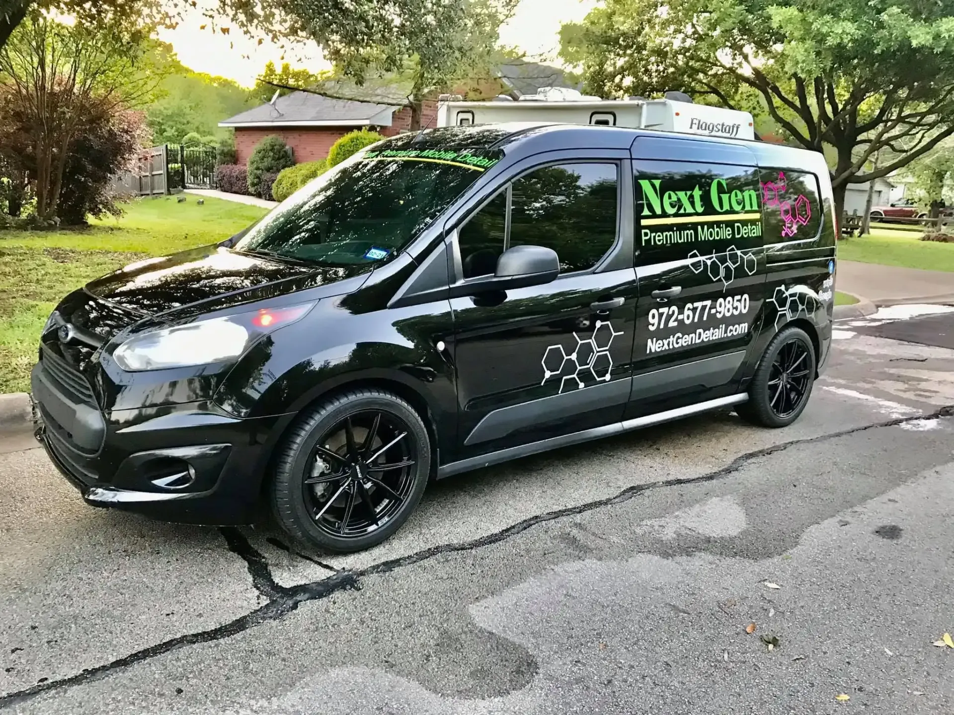 Black van with green business signage parked on a residential street, surrounded by trees and houses Black van with green business signage parked on a residential street, surrounded by trees and houses
