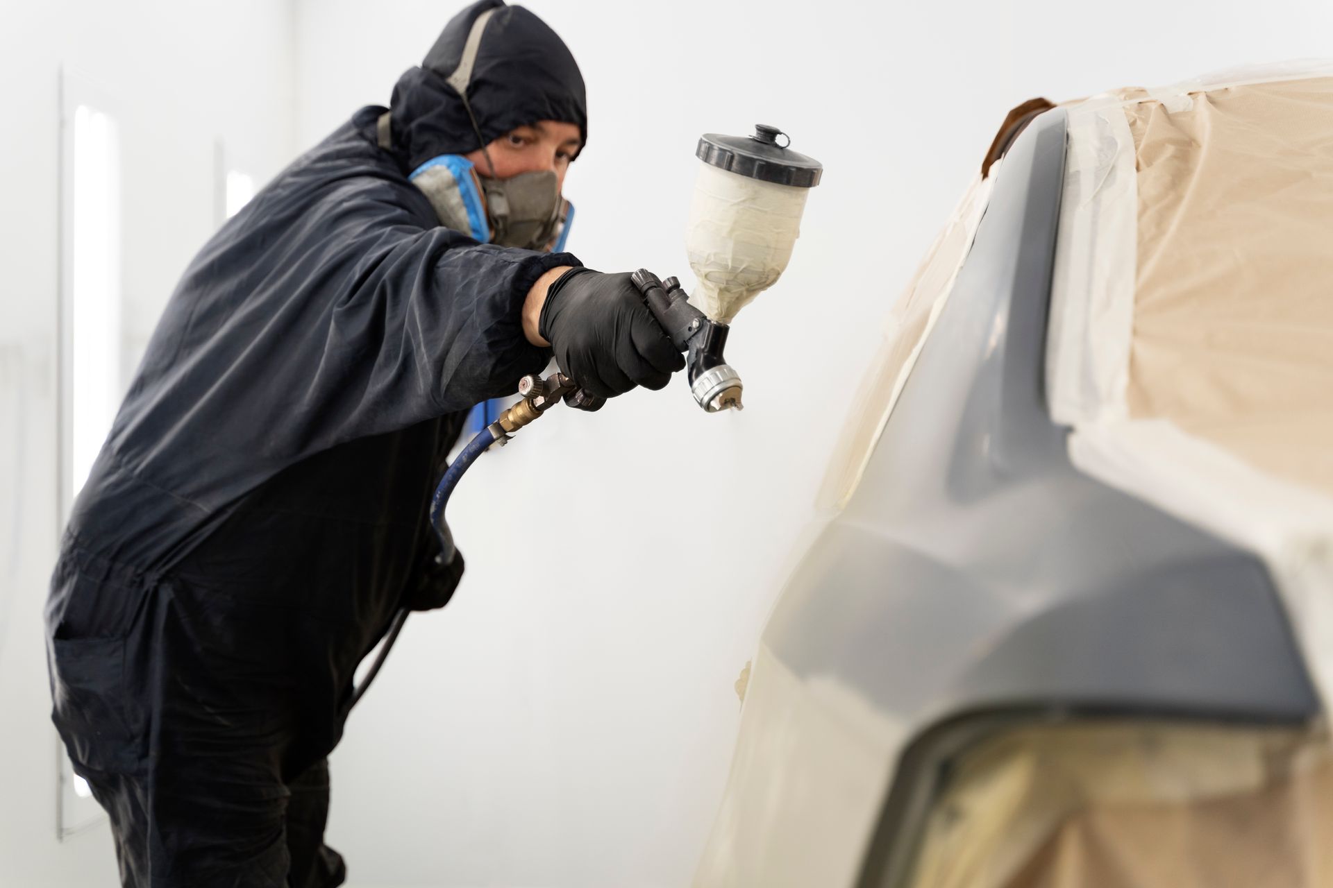 Person in protective gear sprays paint on car body in a spray booth.