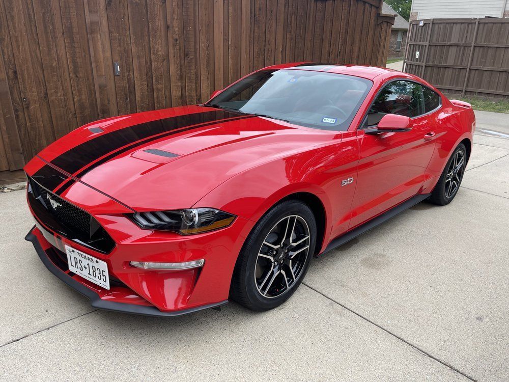 Red Ford Mustang with black racing stripes parked on a driveway.