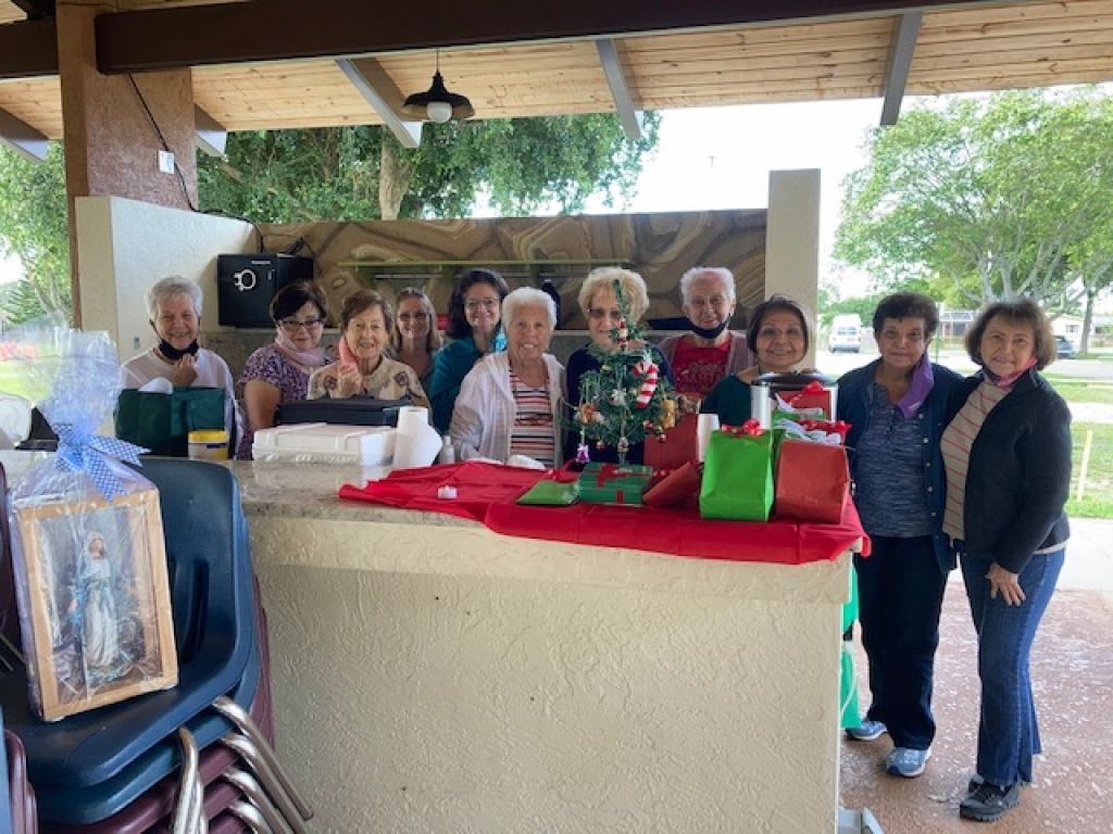 Group of people gathered under a pavilion around a red-covered table with gifts and a decorated tree.