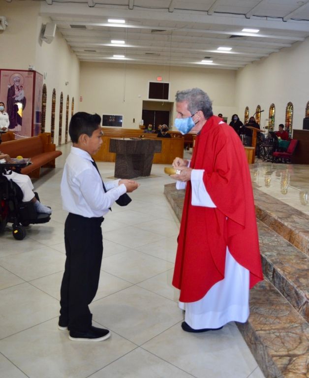 Boy in white shirt faces a red-robed clergy member in a church hall.