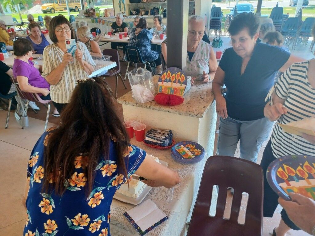 People gathered around a picnic table with snacks and drinks in a covered outdoor pavilion.