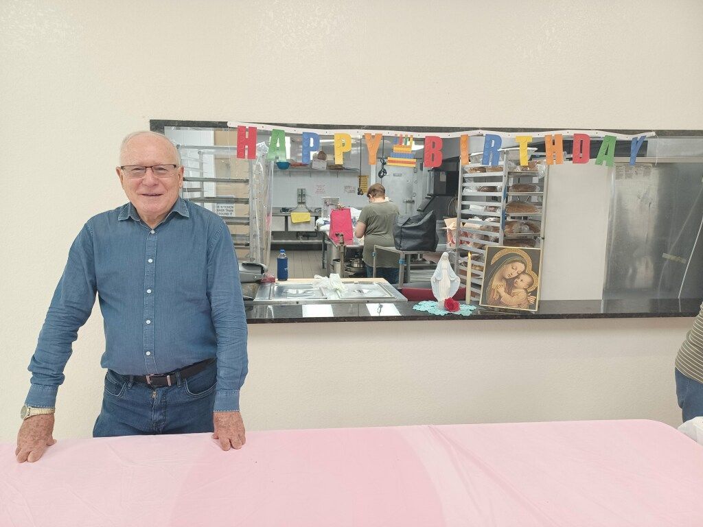Man standing behind a pink-covered table in a room with colorful birthday decorations on the wall