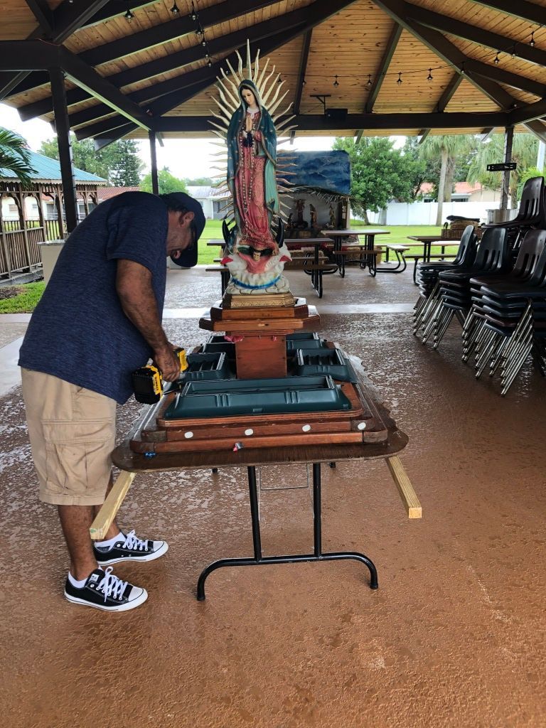 Person bending over a table in an open-air pavilion with rows of stacked chairs behind them.