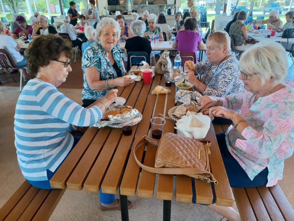 People dining at a long wooden table in a bright cafeteria, eating and talking.