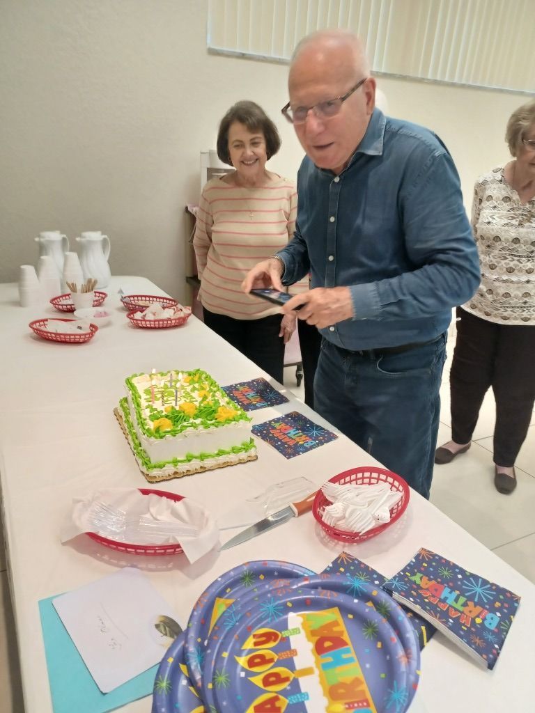 Man cutting a decorated birthday cake at a party table with plates, gifts, and balloons.