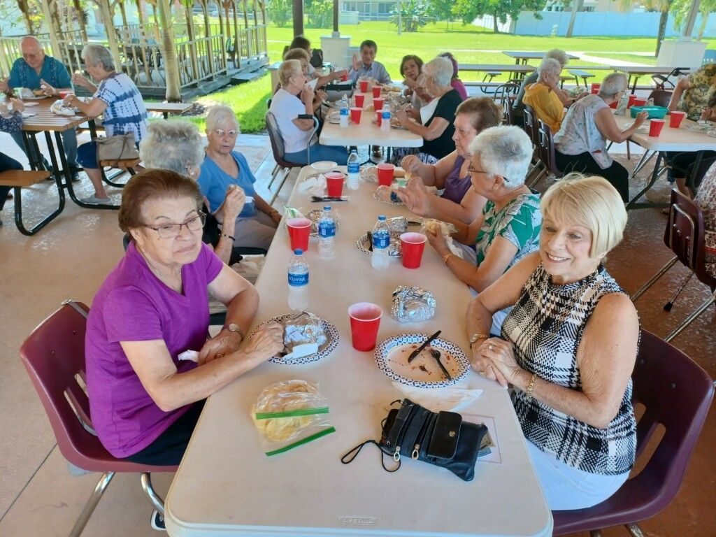 People seated at picnic tables eating and chatting under a pavilion by the water