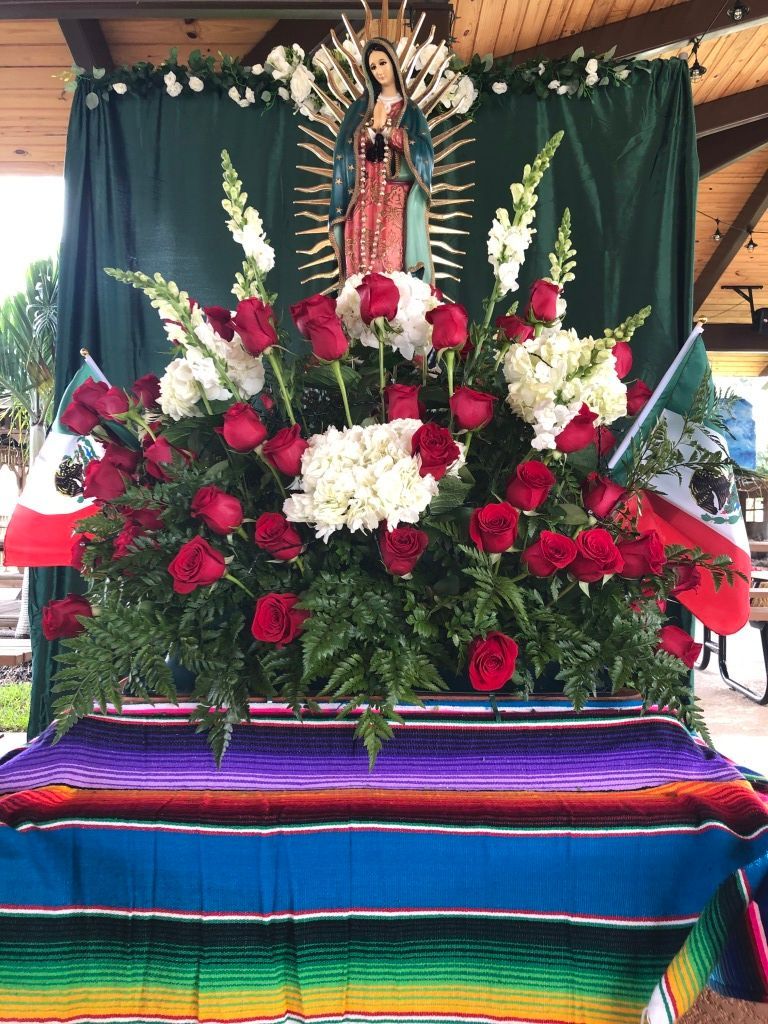 Decorated altar with a statue of the Virgin Mary, red and white flowers, and colorful cloth draping the table