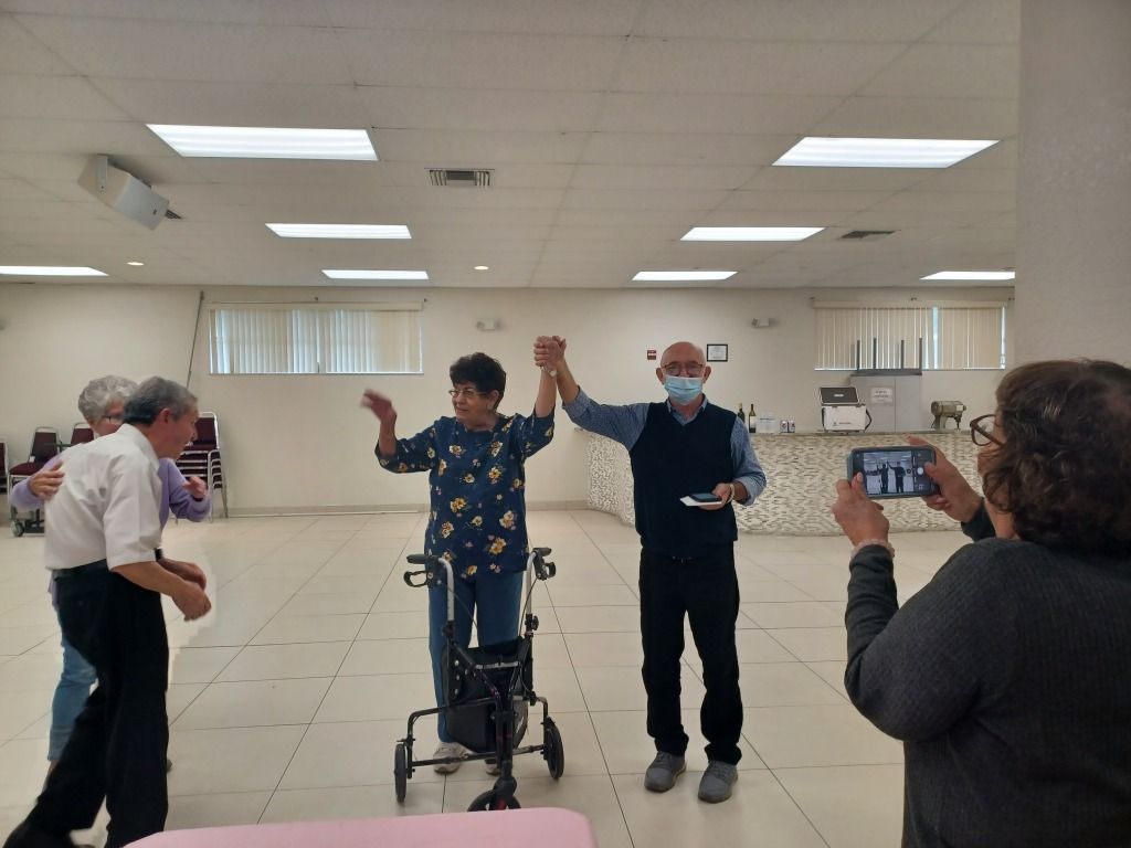 People raising hands in a bright community hall, with one person using a walker and others clapping.
