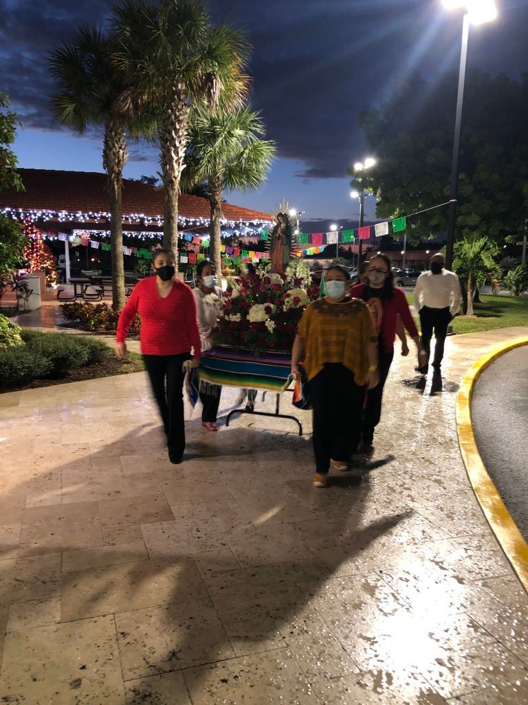 People walking at night on a lit park path, with palm trees and a handcart nearby.