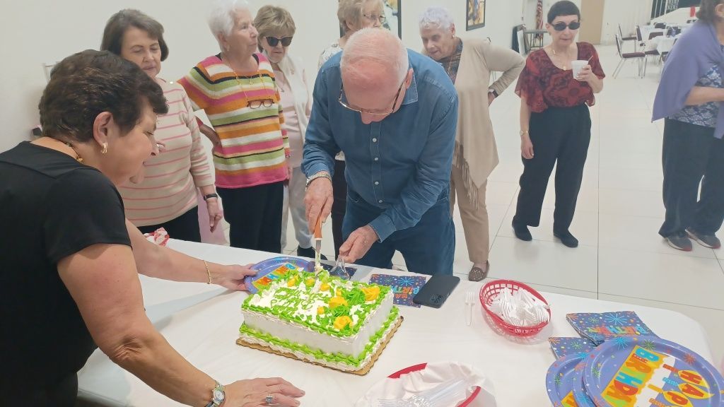 People gathered around a table, cutting a decorated cake at a festive indoor celebration.