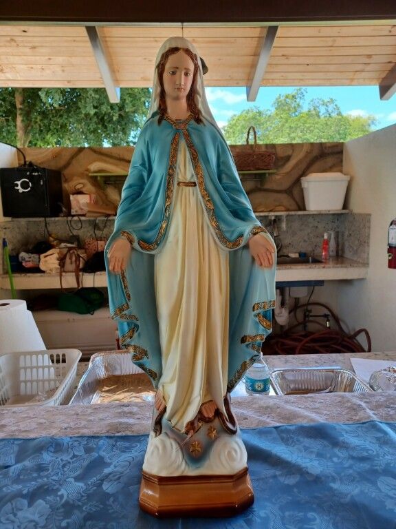 Statue of the Virgin Mary in a blue mantle, standing on a table under a covered outdoor area