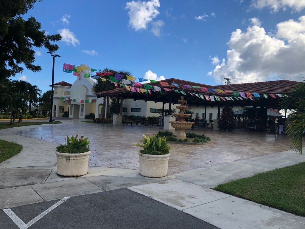Open-air pavilion with colorful bunting, planters, and a fountain on a sunny patio near the water