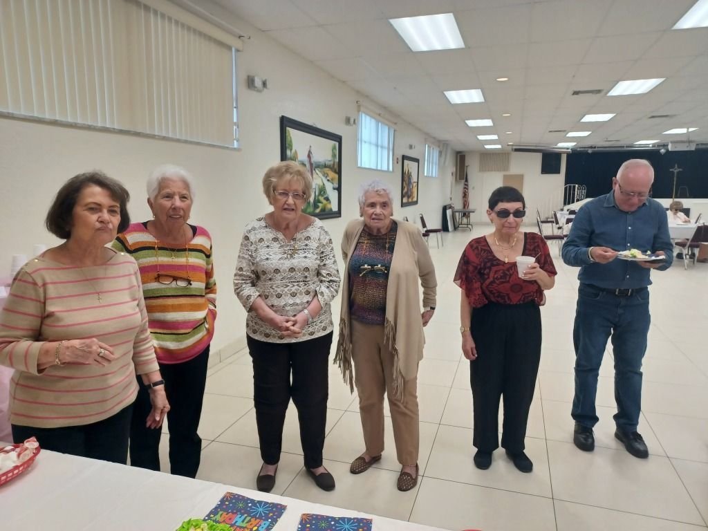 Six people standing in a bright indoor hall, facing the camera during a group activity