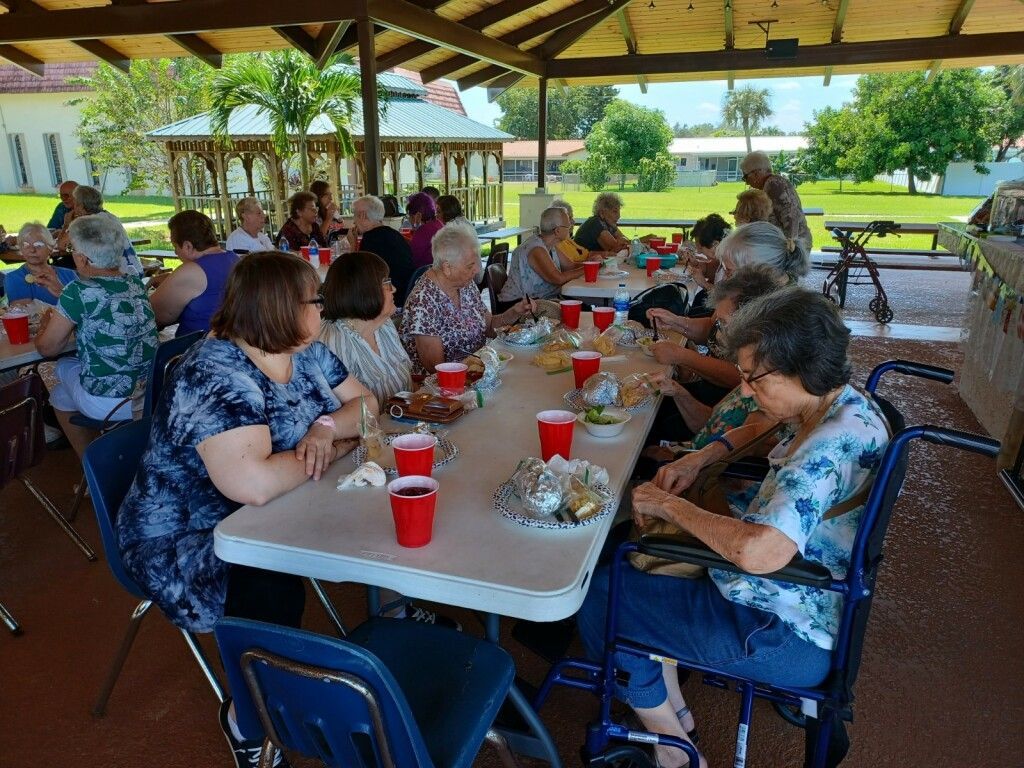 People gathered at picnic tables under a pavilion, eating and talking outdoors.
