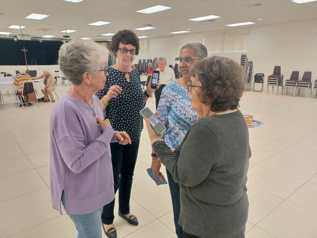 Four people chatting in a bright community hall with chairs in the background.