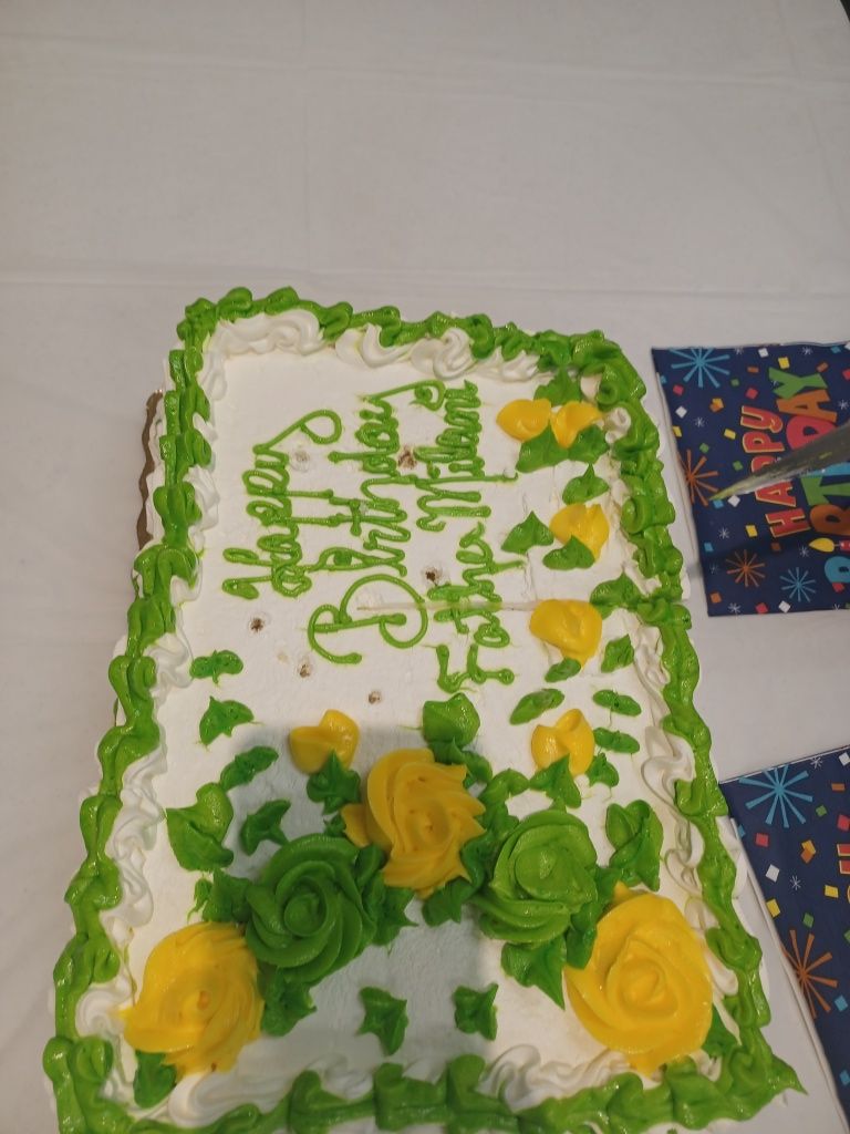 White frosted cake with green icing border and yellow roses on a table with a birthday card