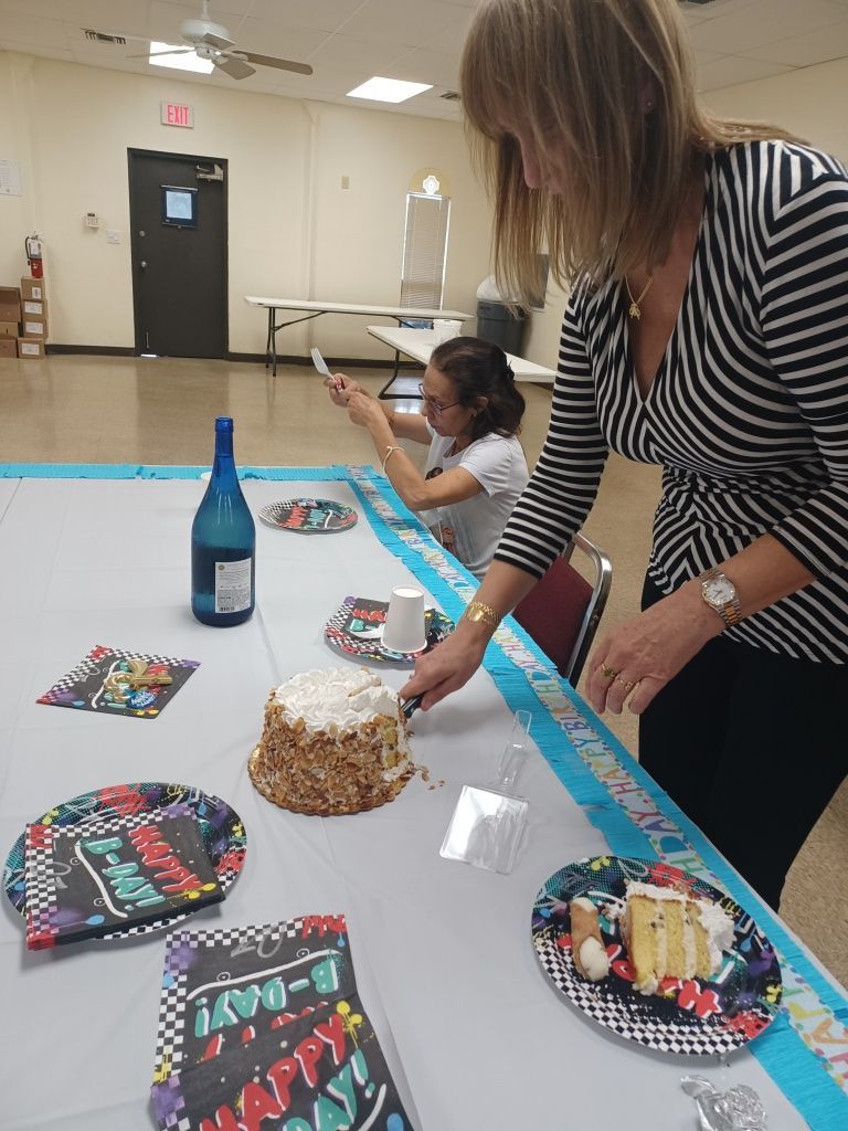Woman cutting a birthday cake at a decorated table in a community room
