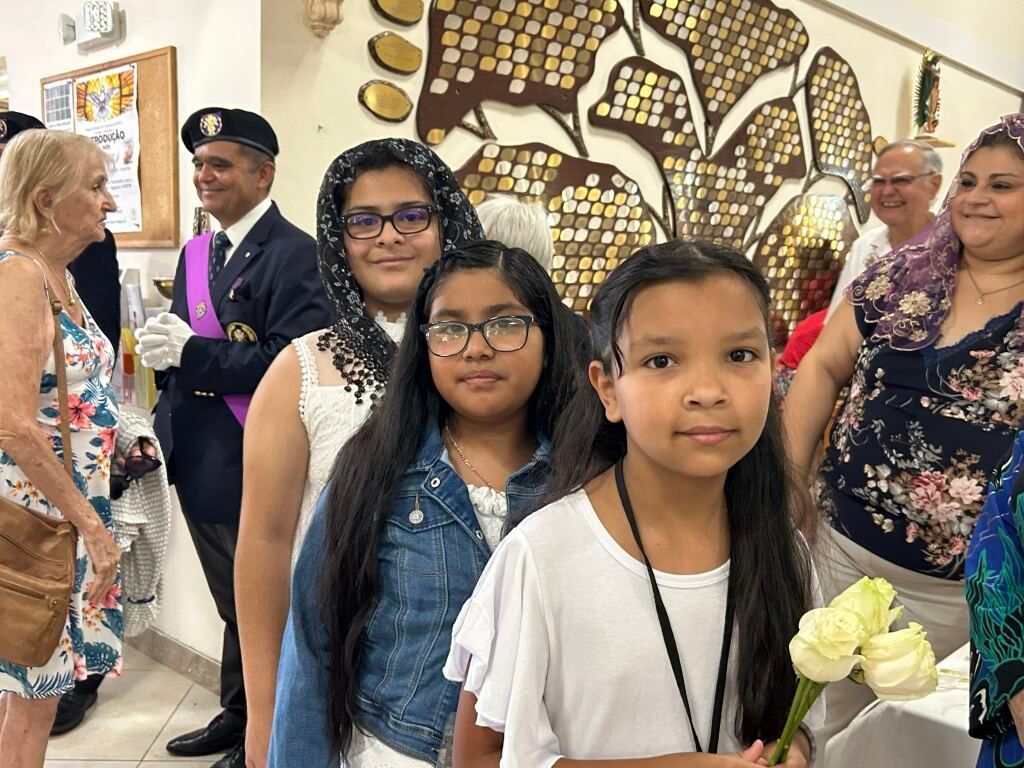 Group of people posing indoors, with two girls in front and a flower-themed wall art display behind them